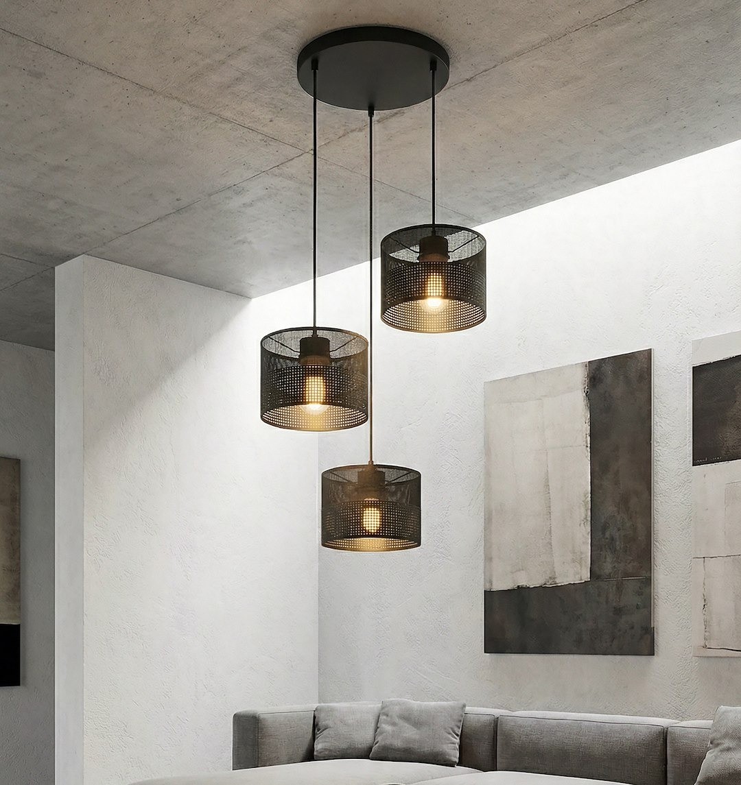 Lampa wisząca Karbon 3xE27 w kolorze czarnym z trzema kloszami w formie siatki, zawieszona na długich linkach, umieszczona w nowoczesnym wnętrzu z jasnymi ścianami i szaro-beżową sofą.