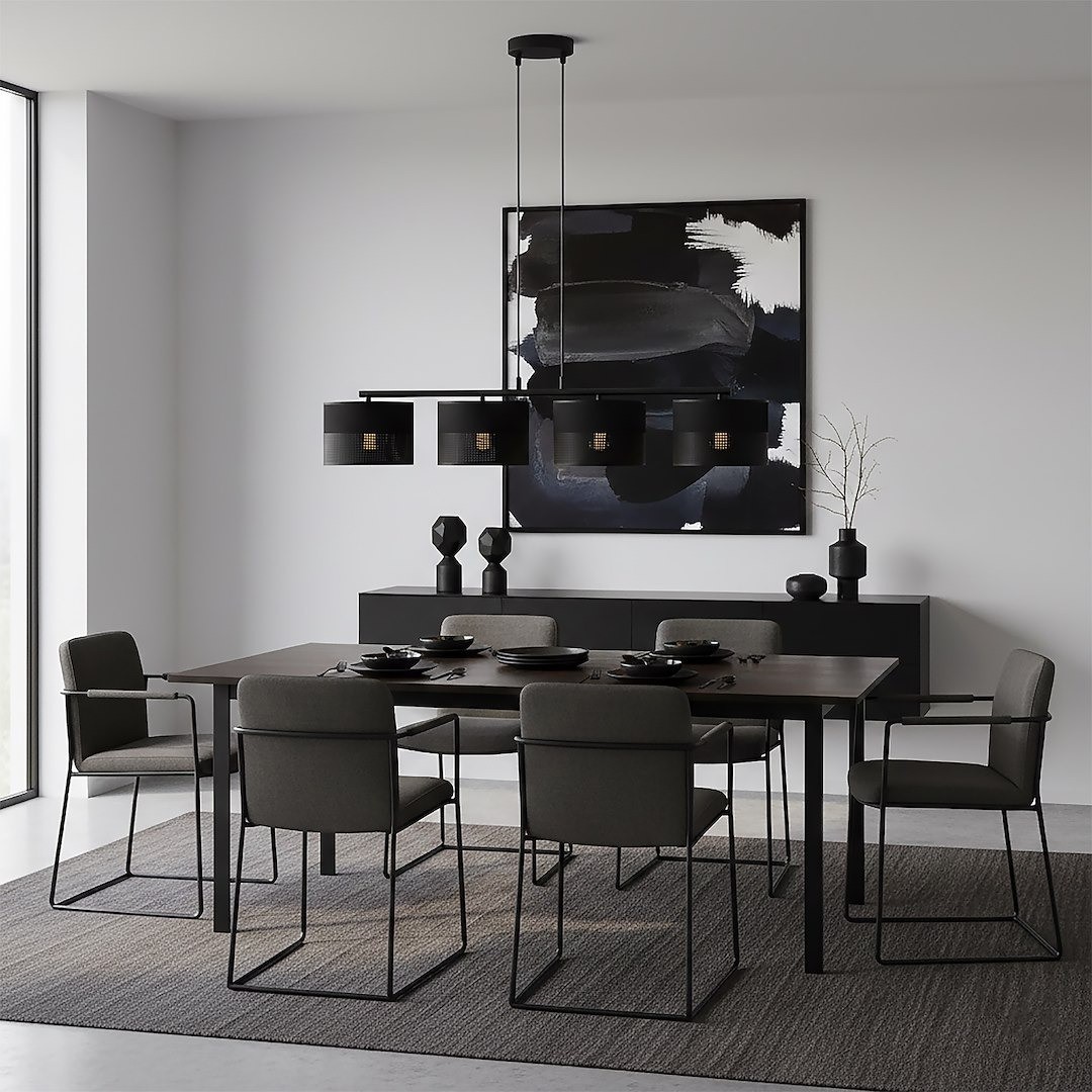 Lampa wisząca Karbon 4xE27 w kolorze czarnym, zawieszona nad stołem w nowoczesnej jadalni. Cztery cylindryczne klosze z siateczkowym wzorem, w otoczeniu szarych krzeseł i dekoracji na bufecie. Tło jasne, minimalistyczne wnętrze.