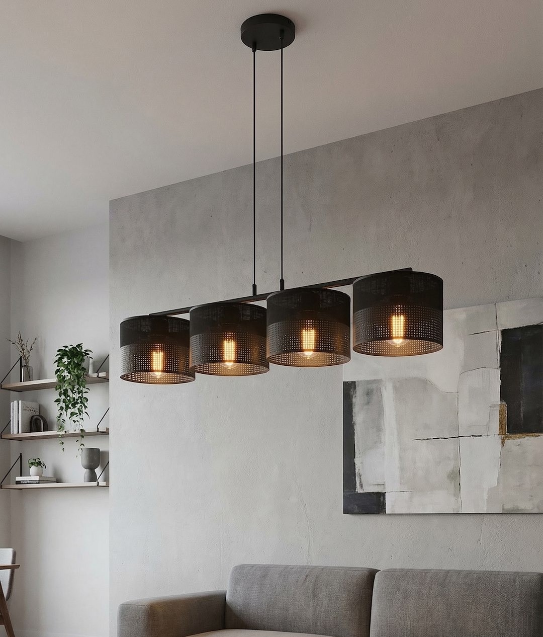 Lampa wisząca Karbon 4xE27 w kolorze czarnym, z czterema cylindrycznymi kloszami o perforowanej strukturze, zawieszona na długim metalowym stelażu. Ujęcie frontalne, lampa umieszczona nad szaro-beżową kanapą w nowoczesnym wnętrzu.