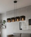 Lampa wisząca Karbon 4xE27 w kolorze czarnym, z czterema cylindrycznymi kloszami o perforowanej strukturze, zawieszona na długim metalowym stelażu. Ujęcie frontalne, lampa umieszczona nad szaro-beżową kanapą w nowoczesnym wnętrzu.