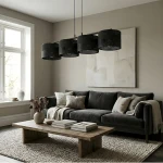 Czarna lampa wisząca Karbon z czterema kloszami E27, zawieszona na długich linkach, w nowoczesnym wnętrzu z szarymi ścianami, obok ciemnoszarej sofy i drewnianego stolika. W tle okno z naturalnym światłem.