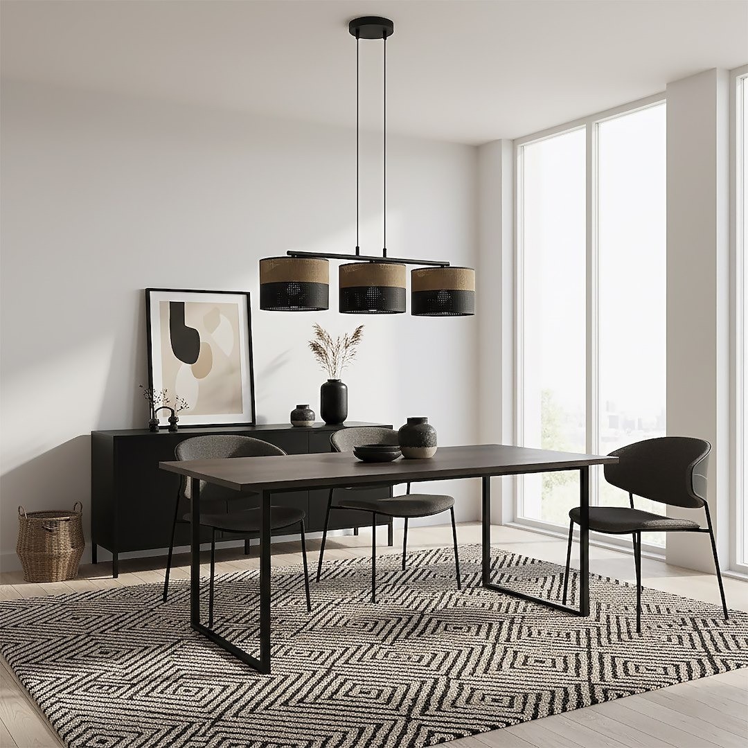 Lampa wisząca Karbon 3xE27 w kolorze czarnym i brązowym z trzema cylindrycznymi kloszami. Umieszczona na długim zwisie, w nowoczesnej aranżacji jadalni z drewnianym stołem i krzesłami, na tle jasnej ściany i dużych okien.