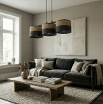 Lampa wisząca Karbon 3xE27 w odcieniach czerni i brązu z trzema okrągłymi kloszami, zawieszona nad drewnianym stołem w jasnym wnętrzu z szarymi ścianami i sofą. Klosze mają ażurowe wykończenie, co podkreśla ich stylowy design.