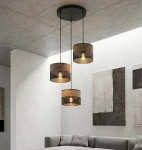 Lampa wisząca Karbon z trzema abażurami w odcieniach czerni i brązu, zawieszona na cienkich linkach z sufitu. Abażury mają perforowaną strukturę, a wewnątrz znajdują się żarówki E27, zapewniając subtelne oświetlenie w nowoczesnym wnętrzu.