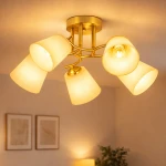 Lampa sufitowa Pafos z pięcioma kloszami w kolorze złotym, z materiału matowego, zamontowana na okrągłej podstawie. Klosze mają lekko stożkowaty kształt, skierowane w różnych kierunkach. Tło jasne, z subtelnym oświetleniem w pomieszczeniu.
