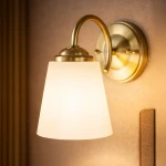 Kinkiet Pafos 1xE27 w złotym wykończeniu, z białym kloszem w kształcie stożka. Montowany na ścianie, z widoczną metalową podstawą i zakrzywioną rączką. Oświetlenie w subtelnym, eleganckim stylu, idealne do wnętrz.