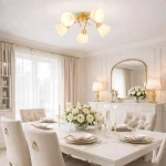 Lampa sufitowa Clara 5xE27 w kolorze złotym, z pięcioma kloszami w kształcie stożka, zamontowana na suficie. Oświetlenie w eleganckim wnętrzu jadalni z jasnymi zasłonami i stołem nakrytym na przyjęcie.
