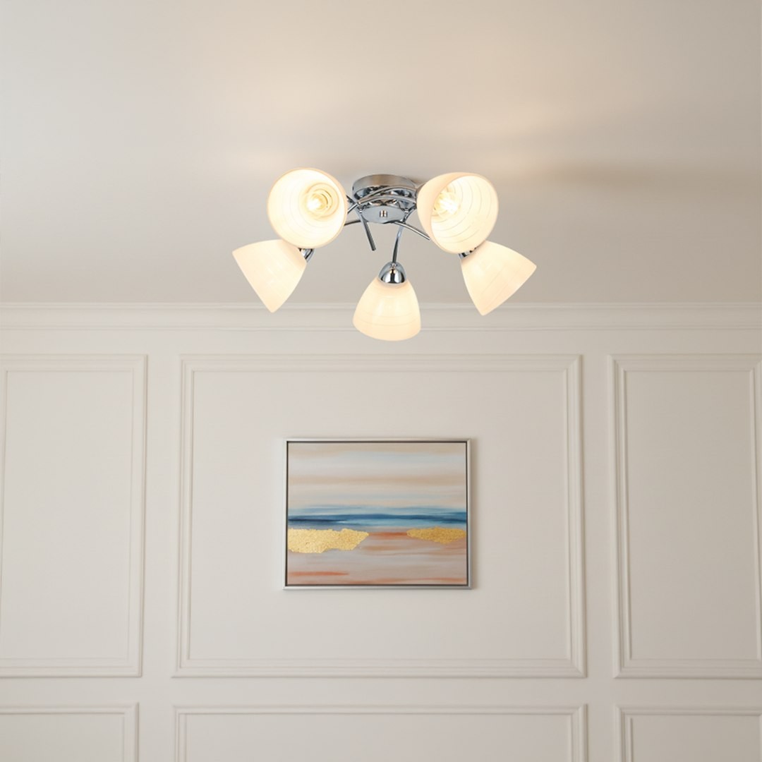 Lampa sufitowa Clara z pięcioma kloszami E27 w chromowanej oprawie. Klosze w kształcie stożków w kolorze białym, zamontowane na okrągłej podstawie. Produkt umieszczony na białym suficie, w tle widoczny obraz z abstrakcyjnym motywem.
