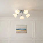 Lampa sufitowa Clara z pięcioma kloszami E27 w chromowanej oprawie. Klosze w kształcie stożków w kolorze białym, zamontowane na okrągłej podstawie. Produkt umieszczony na białym suficie, w tle widoczny obraz z abstrakcyjnym motywem.