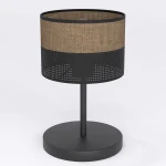 Lampka stołowa Karbon E27 w kolorze czarnym z brązowym abażurem. Okrągła podstawa i metalowy stelaż z perforowaną dolną częścią. Abażur wykonany z tekstylnego materiału, zapewniającego ciepłe światło. Ujęcie z boku, na jednolitym białym tle.