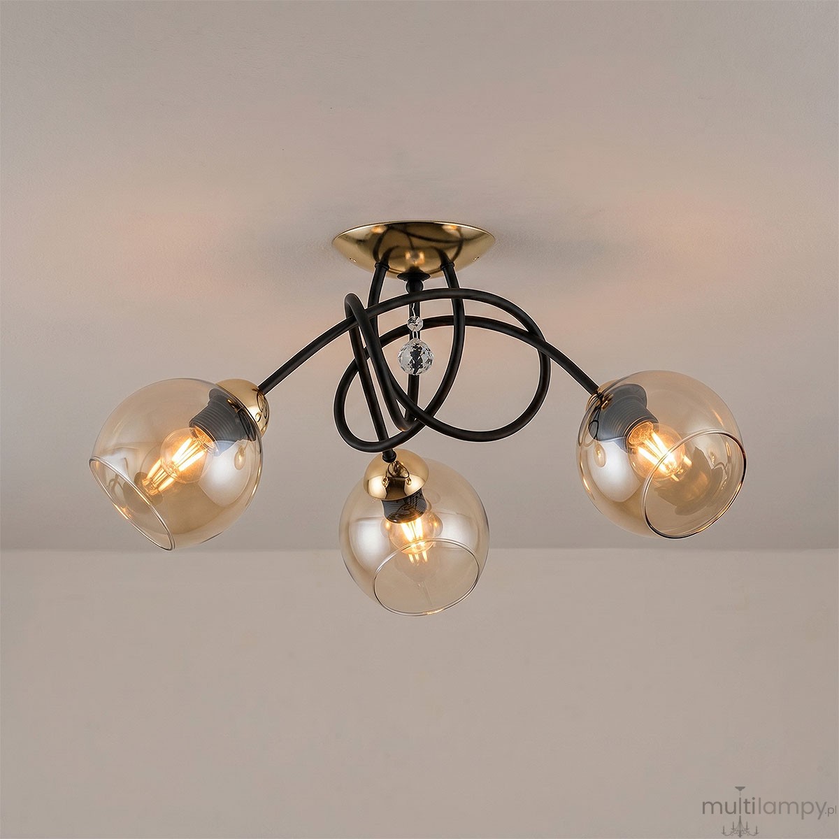 Modena Black lampa sufitowa 3-punktowa w kolorze czarnym i złotym, z trzema przezroczystymi kloszami w kształcie kul. Lampa ma czarne przewody i złoty uchwyt sufitowy, z dekoracyjnym kryształkiem na środku.