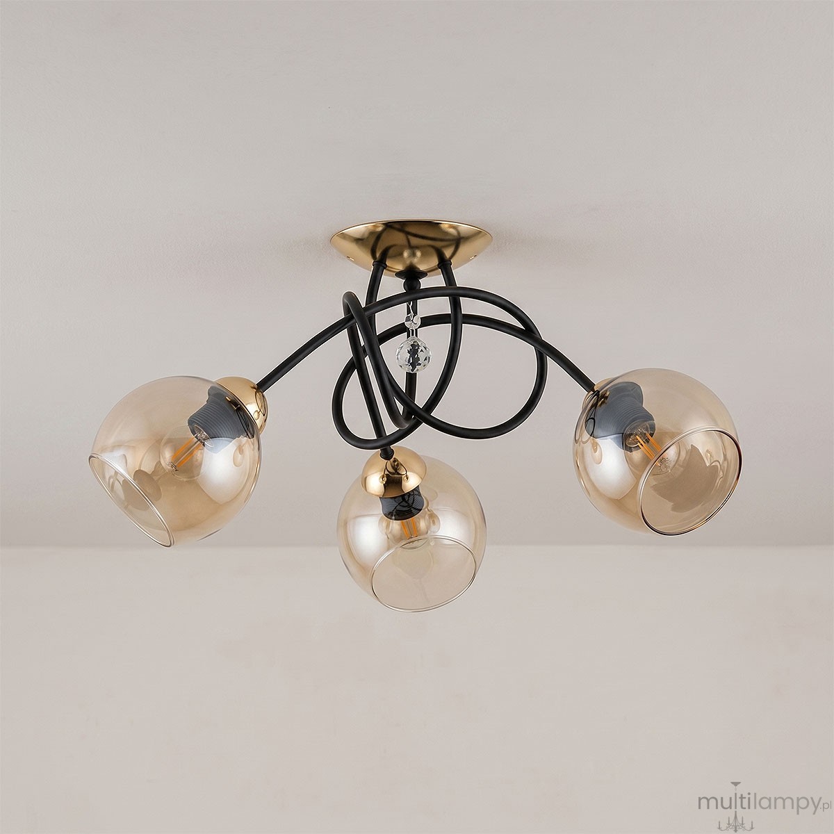 Modena Black lampa sufitowa 3-punktowa w kolorze czarnym i złotym, z trzema przezroczystymi kloszami w kształcie kul. Lampa ma czarne przewody i złoty uchwyt sufitowy, z dekoracyjnym kryształkiem na środku.