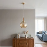 Lampa wisząca Hetty z pojedynczym gniazdem E27, w kolorze złotym i drewnianym. Okrągły klosz ze szkła w odcieniu bursztynowym, zawieszona na przezroczystym przewodzie. Stylowy element oświetleniowy idealny do nowoczesnych wnętrz.