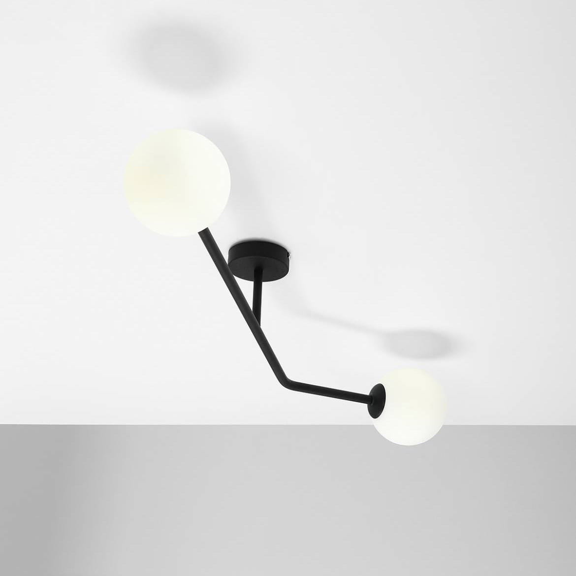 Czarna lampa sufitowa 2-punktowa Pure z dwoma białymi, okrągłymi kloszami. Ujęcie z góry, pokazujące stylowy kształt oraz mocowanie do sufitu. Lampa ma minimalistyczny design, umieszczona na białym tle.