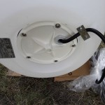 Biała lampa ogrodowa Cumulus S z gniazdem E27, widok od spodu. Na zdjęciu widoczna podstawa z otworami montażowymi oraz przewód elektryczny wychodzący z obudowy. Tło naturalne, trawiaste.