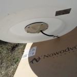 Lampa ogrodowa Cumulus L w kolorze białym, z oprawą na żarówkę E27. Widok z dołu ukazujący mocowanie oraz przewód elektryczny. Tło stanowi karton z logo „Nowodvorski Lighting”.