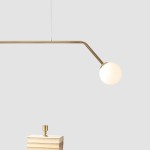 Lampa wisząca Pure 2-punktowa w kolorze złotym, z metalowym ramieniem z jedną oprawą w kształcie kuli z mlecznego szkła. Ujęcie frontalne, z zawieszeniem nad stosem książek. Prosty, nowoczesny design, odpowiednia do różnych aranżacji wnętrz.
