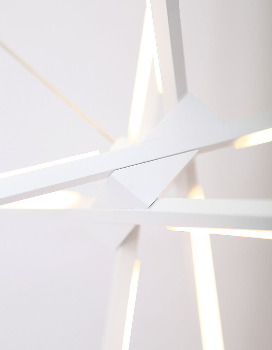 Biała lampa wisząca Spider LED o trzech punktach świetlnych. Zbliżenie na strukturę lampy z geometrycznymi kształtami i wbudowanym oświetleniem LED. Elementy są matowe, a światło emituje się z wąskich szczelin. Tło jasne, minimalistyczne.