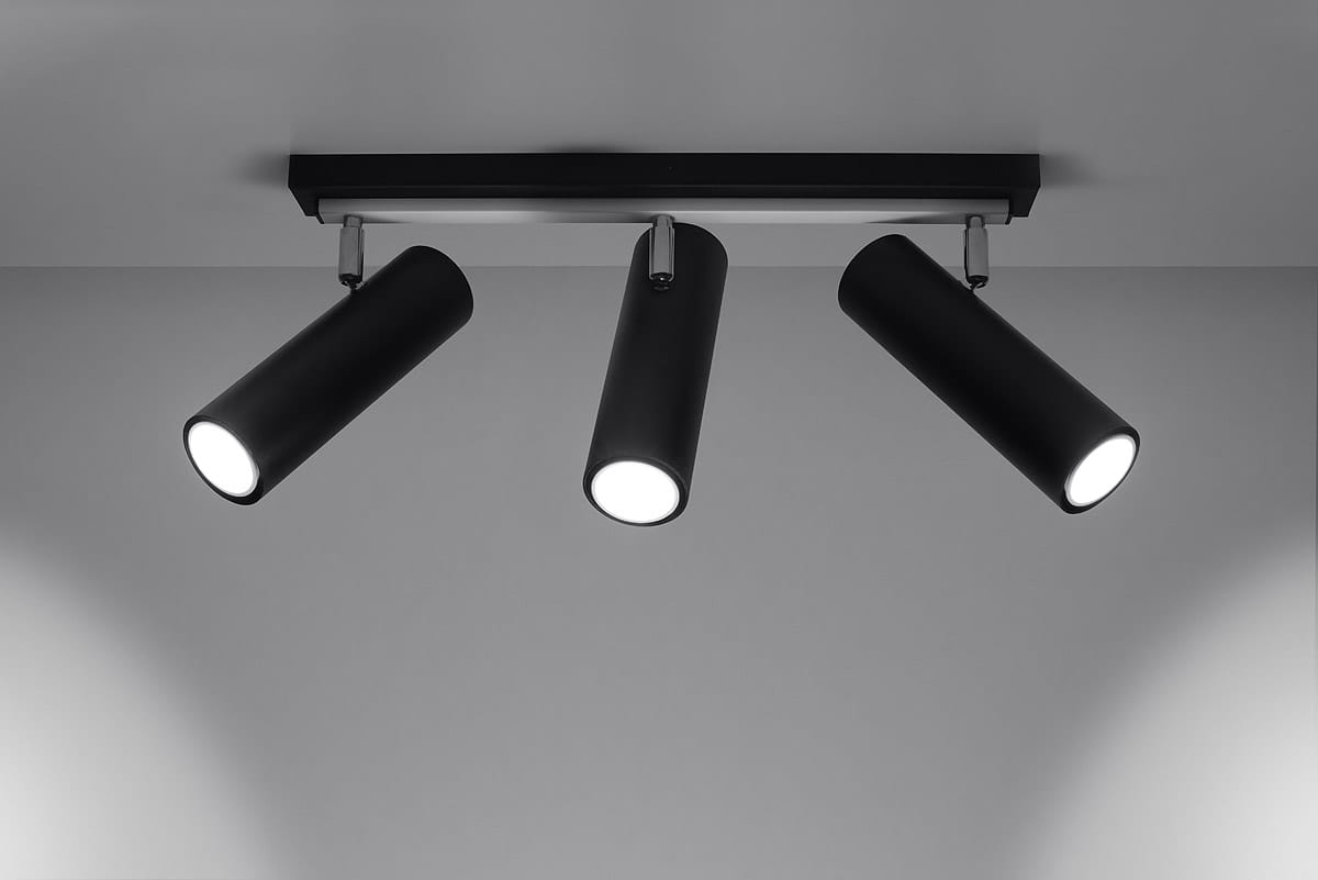 Trzypunktowa lampa sufitowa Direzione w kolorze czarnym, z cylindrycznymi reflektorami, zamontowana na prostokątnej podstawie. Reflektory są skierowane w różne strony, co umożliwia kierunkowe oświetlenie. Tło jasne, minimalistyczne.
