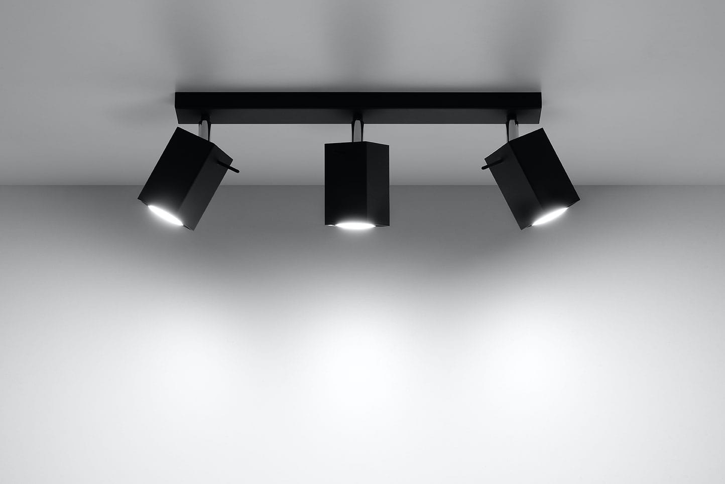 Czarna lampa sufitowa Merida z trzema punktami świetlnymi, zamontowana na prostokątnej podstawie. Reflektory w kształcie prostopadłościanów skierowane w różne strony, idealna do oświetlenia wnętrz. Tło jasne, minimalistyczne.