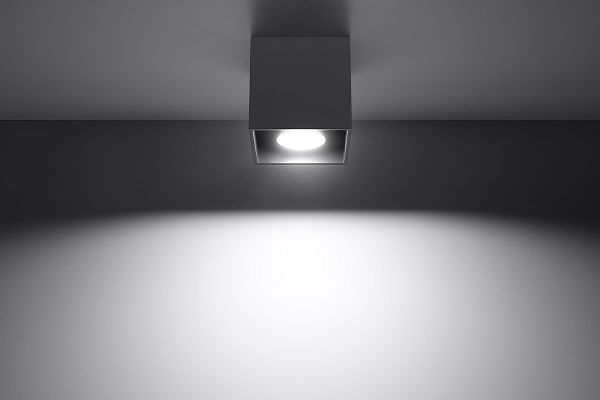 Antracytowa lampa sufitowa 1-punktowa Quad, umieszczona na suficie, kwadratowa obudowa z widoczną żarówką, emitująca światło na ścianę. Prosty design i minimalistyczny styl, tło jednolite, jasne.