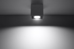 Antracytowa lampa sufitowa 1-punktowa Quad, umieszczona na suficie, kwadratowa obudowa z widoczną żarówką, emitująca światło na ścianę. Prosty design i minimalistyczny styl, tło jednolite, jasne.