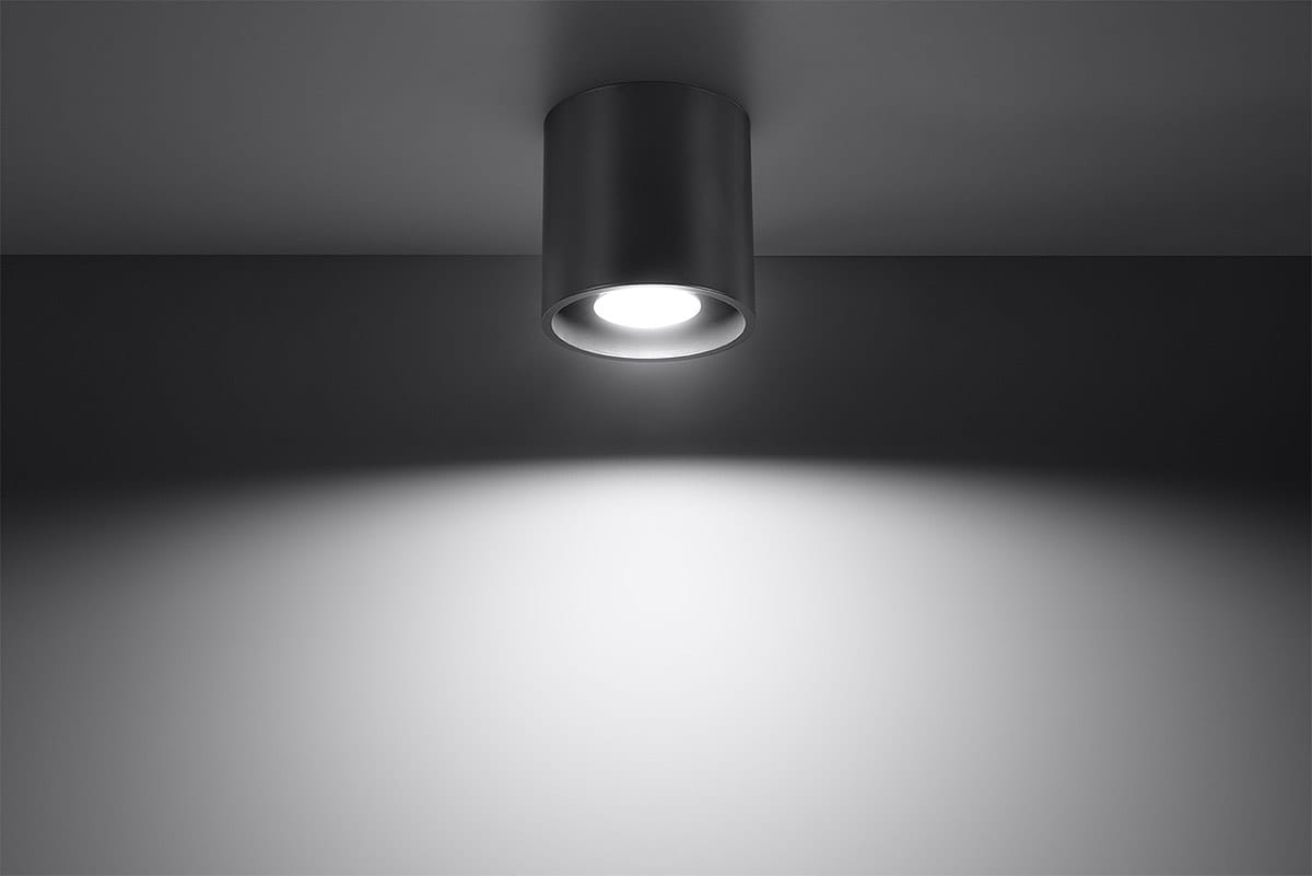 Lampa sufitowa Orbis 1-punktowa w kolorze antracytowym, montowana na suficie, z widocznym źródłem światła. Kształt cylindryczny, z minimalistycznym designem, rzuca jasne światło na ścianę w tle.