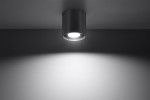 Lampa sufitowa Orbis 1-punktowa w kolorze antracytowym, montowana na suficie, z widocznym źródłem światła. Kształt cylindryczny, z minimalistycznym designem, rzuca jasne światło na ścianę w tle.
