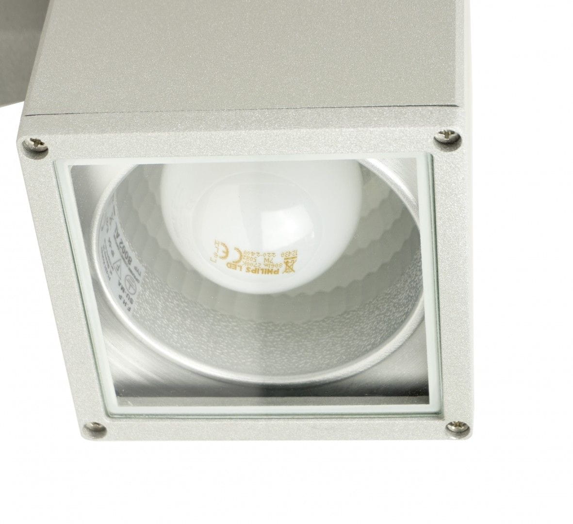 Kinkiet elewacyjny Adela 2-punktowy w kolorze aluminium. Widoczny klosz z przezroczystego szkła, w środku żarówka LED. Kąt ujęcia z góry, podkreślający prostokątny kształt i fakturę powierzchni. Elementy montażowe widoczne w rogu.