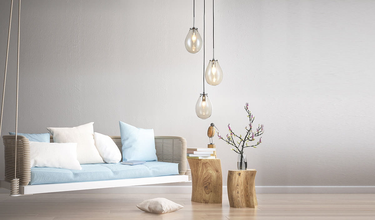 Lampa wisząca 3-punktowa LP-1214/3P z przezroczystymi kloszami w kształcie kropli, zawieszona na cienkich, czarnych linkach. W tle jasna ściana, sofa z błękitnym siedziskiem i poduszkami, drewniane stoliki oraz gałązka w wazonie.