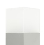 Lampa stojąca ogrodowa Cube, 1-punktowa, wykonana z aluminium. Posiada prostokątną, matową podstawę w kolorze szarym oraz górną część z mlecznego szkła, emitującą światło. Ujęcie z góry, eksponujące kształt i fakturę materiałów.
