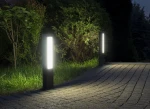Lampa stojąca ogrodowa Evo H50 z dwoma źródłami LED 12W, 4000K, w kolorze ciemnego popielu. Prezentowana w zewnętrznym otoczeniu, oświetla ścieżkę. Posiada prostokątny kształt i matowe klosze, umieszczona na ciemnej podstawie.