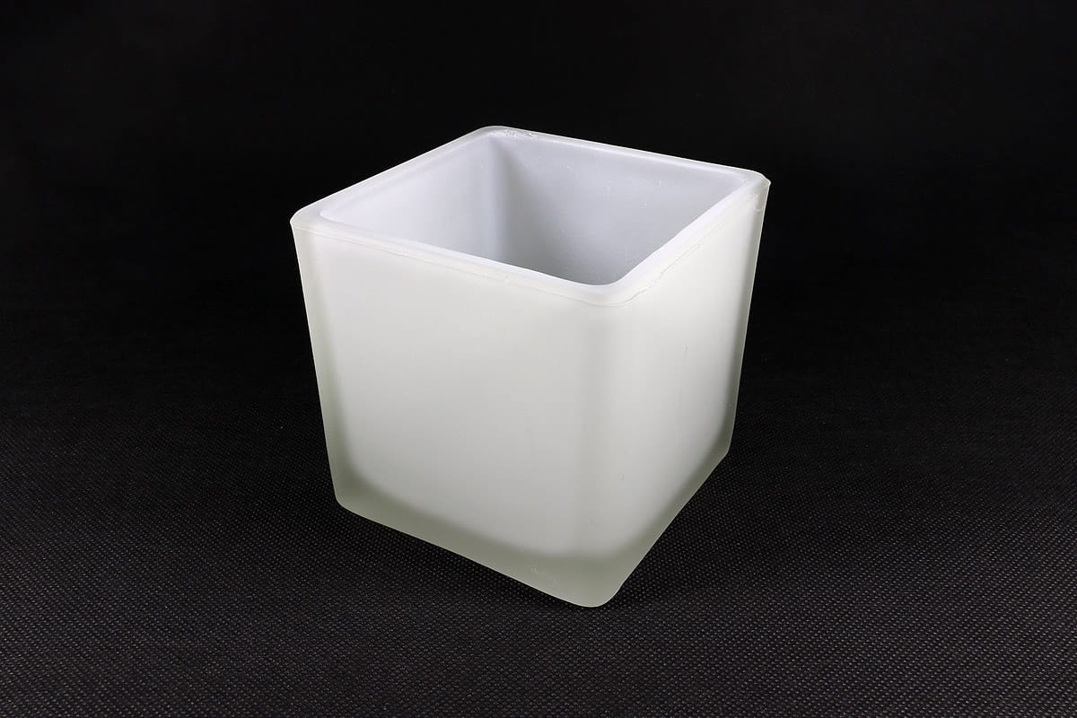 Klosz szklany w kształcie kostki, o wymiarach 100x100 mm, w białym, matowym kolorze. Ujęcie z boku, z widocznymi prostymi krawędziami i gładką powierzchnią. Produkt leżący na ciemnym tle, bez dodatkowych elementów.