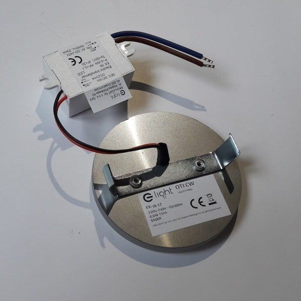 Oti LED oprawa schodowa 230V z ciepłą barwą światła 3000K. Metalowa, okrągła podstawa z widocznym uchwytem montażowym i przewodami. Zasilacz w białej obudowie z oznaczeniami. Produkt przeznaczony do oświetlenia schodów.