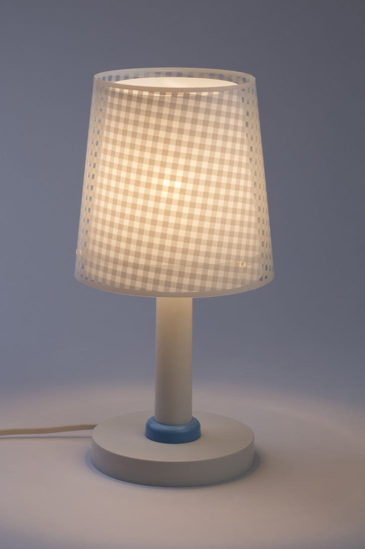 Lampka nocna Vichy 1-punktowa z białym kloszem w kratkę i niebieskim detalem na podstawie. Ustawiona na okrągłej, białej podstawie, emituje ciepłe światło. Klosz ma lekko przezroczystą teksturę, co podkreśla jego delikatny design.