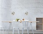 Lampa wisząca Carera Cromo S w chromowanej obudowie, o okrągłym kształcie, zawieszona nad drewnianym stołem. W tle widoczne białe krzesła i minimalistyczne aranżacje z roślinami oraz dekoracjami. Tło w stonowanej, szarej kolorystyce.