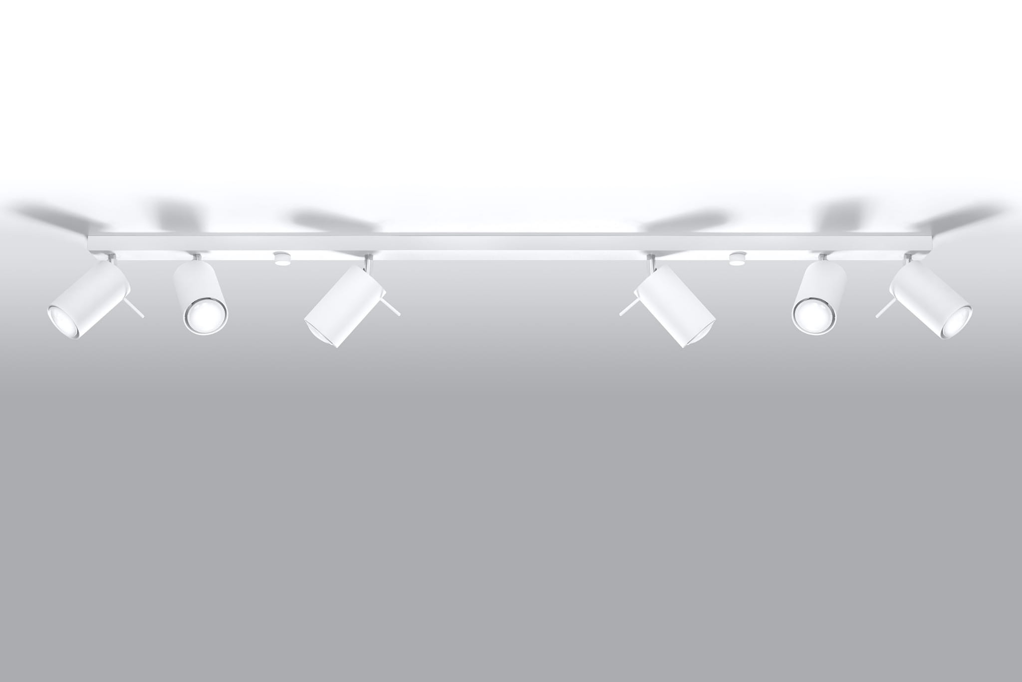 Biała lampa sufitowa typu spot z sześcioma punktami świetlnymi, zamontowana na prostokątnej ramie. Reflektory w kształcie cylindrów, skierowane w różnych kierunkach, na gładkim, jasnym tle.
