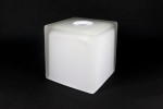 Klosz szklany w kształcie kostki o wymiarach 120x120 mm, wykonany z matowego białego szkła. Posiada okrągły otwór na górze. Produkt stoi na płaskiej powierzchni, na jednolitym ciemnym tle.