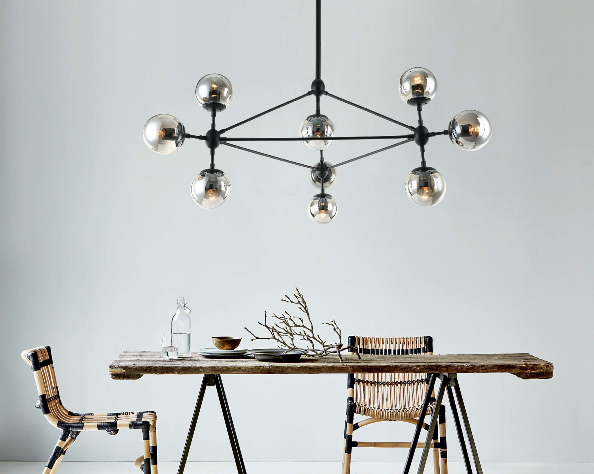 Lampa wisząca Bao Neo Fume z 10 punktami świetlnymi, z czarnym metalowym stelażem i przezroczystymi kulistymi kloszami. Zawieszona nad drewnianym stołem w aranżacji jadalni, w otoczeniu krzeseł z plecionki. Tło jasne, minimalistyczne.