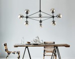 Lampa wisząca Bao Neo Fume z 10 punktami świetlnymi, z czarnym metalowym stelażem i przezroczystymi kulistymi kloszami. Zawieszona nad drewnianym stołem w aranżacji jadalni, w otoczeniu krzeseł z plecionki. Tło jasne, minimalistyczne.