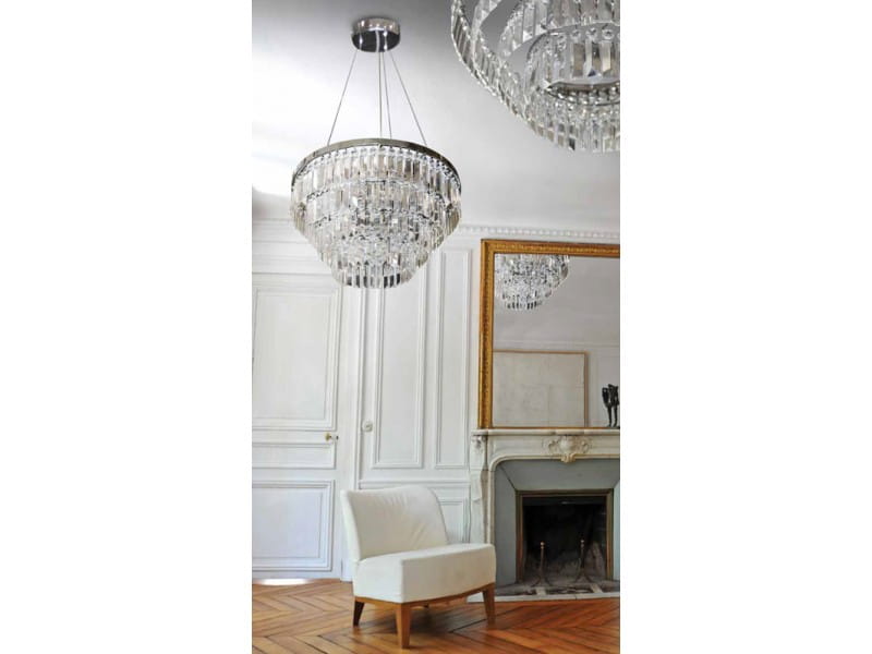 Lampa wisząca Salerno 5-punktowa AZ2107, z metalowym wykończeniem w kolorze srebrnym, ozdobiona kryształowymi elementami. Zawieszona centralnie w jasnym wnętrzu, nad białym fotelem, w eleganckim otoczeniu z lustrami i klasycznymi detalami.