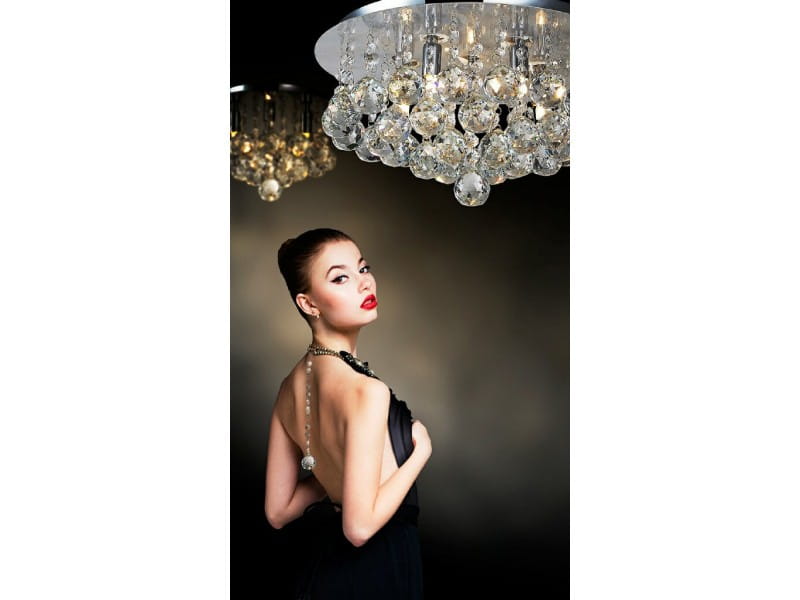 Lampa sufitowa Bolla D58 w kształcie okrągłym z 10 punktami świetlnymi, ozdobiona kryształowymi elementami, zawieszona w eleganckim wnętrzu. Widoczna lśniąca powierzchnia i dekoracyjne refleksy na tle ciemnej ściany.