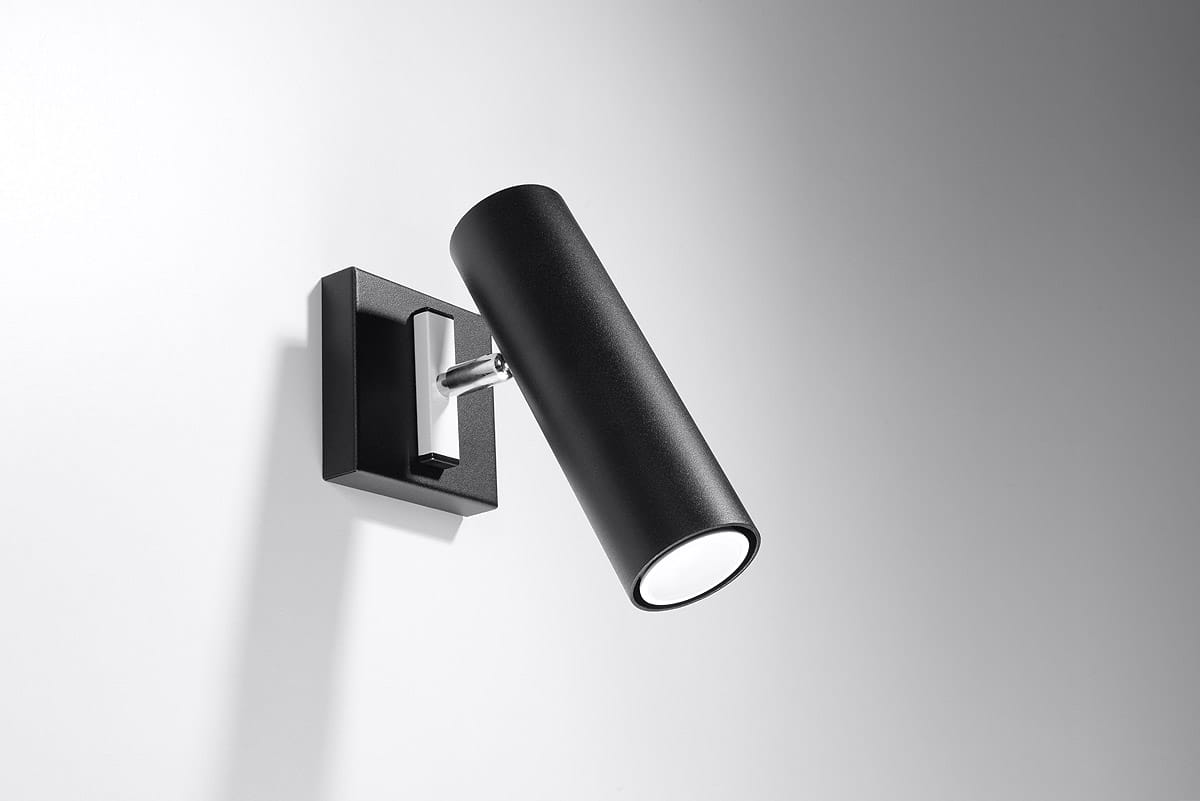 Kinkiet Direzione 1-punktowy w kolorze czarnym z cylindryczną oprawą. Montowany na ścianie w prostokątnej, matowej podstawie. Ujęcie z boku, podkreślające minimalistyczny design i chromowany detal mocujący.