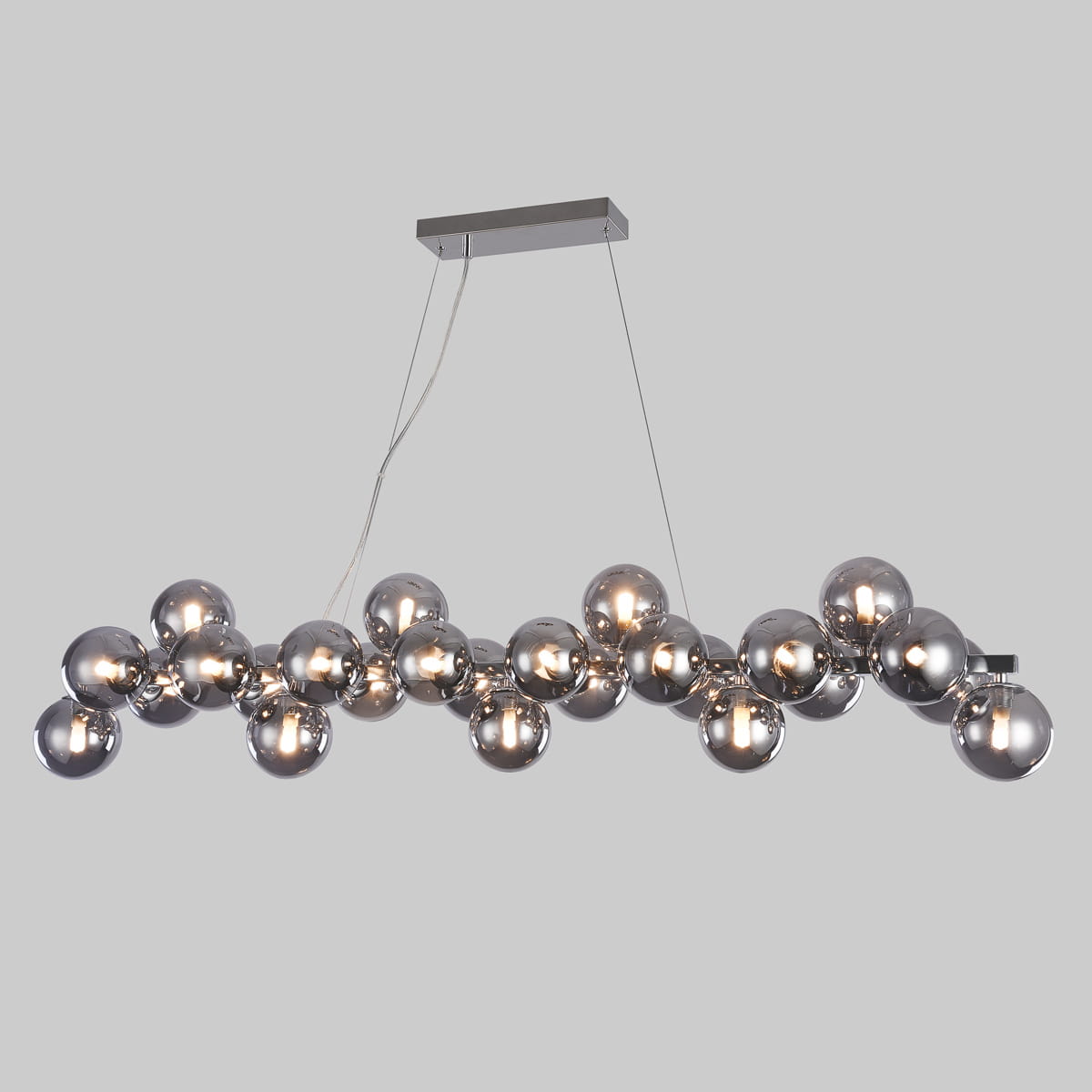 Lampa wisząca Cabella 25-punktowa z dymionymi kulami, umieszczona na prostokątnej, metalowej podstawie. Kule w różnych rozmiarach, w kolorze dymnym, z widocznymi źródłami światła. Zawieszona na cienkich linkach, w nowoczesnym stylu.