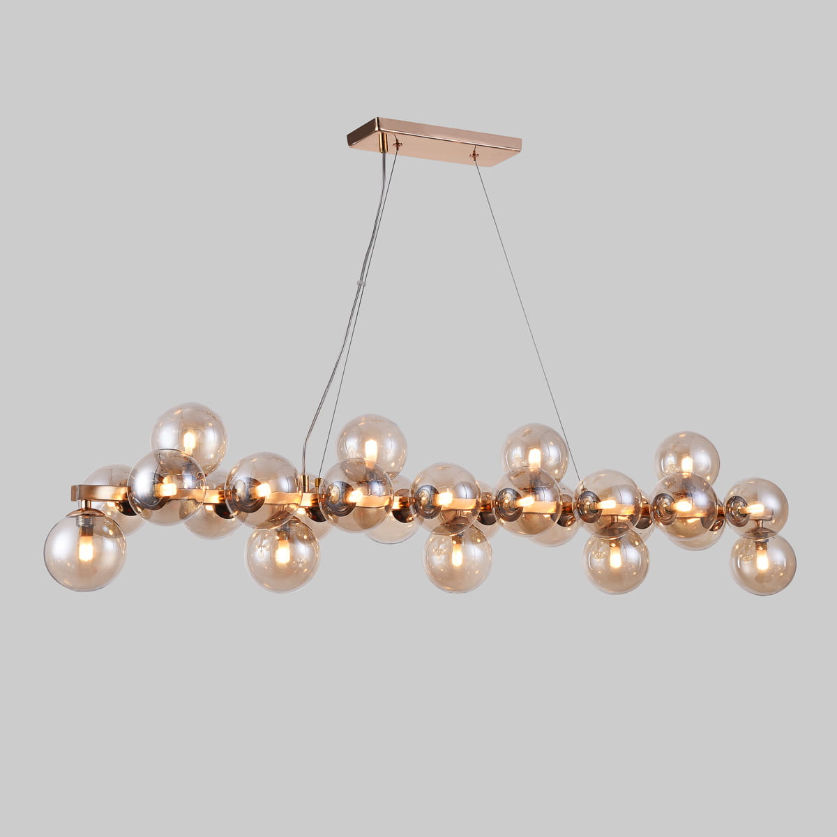 Lampa wisząca Cabella 25-punktowa w kolorze koniakowym, z metalową konstrukcją i przezroczystymi szklanymi kloszami. Ułożona poziomo, zawieszona na cienkich linkach, z prostokątnym, złotym uchwytem montażowym.