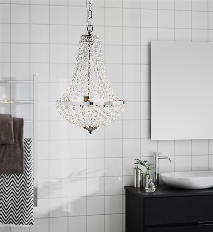 Lampa wisząca Granso 2-punktowa w chromie, z kryształowymi dekoracjami. Zawieszona na łańcuchu, w łazience z białymi kafelkami. W tle czarna szafka z umywalką i lustrem. IP44, odpowiednia do wilgotnych pomieszczeń.