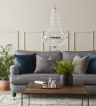 Lampa wisząca Granso 2-punktowa w kolorze chromu, z przezroczystymi kryształami, zawieszona nad szaro-niebieską sofą. W tle widoczne rośliny, drewniany stół z dekoracjami oraz poduszki w różnych odcieniach.