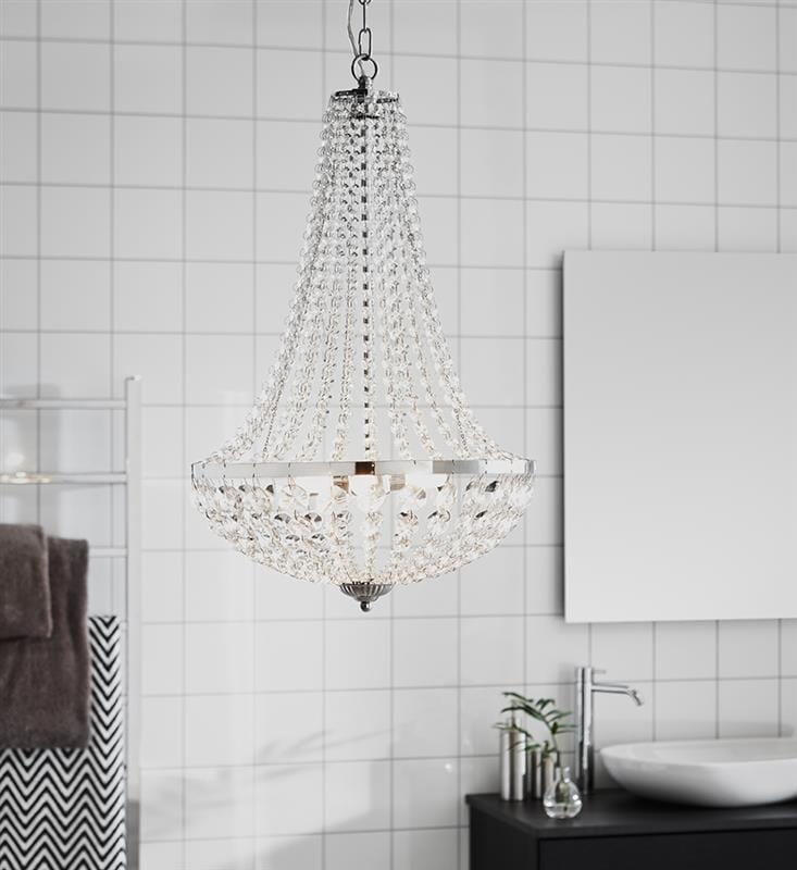 Lampa wisząca Granso 3-punktowa, chromowana, z przezroczystymi kryształkami, w kształcie stożka. Zawieszona na łańcuchu w jasnym wnętrzu z białymi kafelkami. Widoczne detale: błyszczące wykończenie, elegancki design.