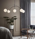 Lampa wisząca Heaven 5-punktowa w stalowej oprawie, posiada pięć okrągłych kloszy z mlecznego szkła, zawieszona na łukowatych ramionach. Umieszczona w nowoczesnym wnętrzu z rośliną w doniczce i szaro-beżowymi zasłonami.