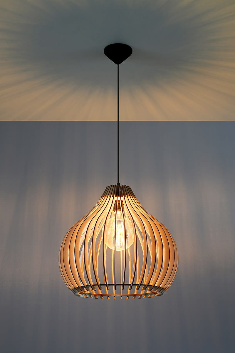 Lampa wisząca Aprilla SL.0639, 1-punktowa, o organicznym kształcie z drewna, w kolorze naturalnym. Zawieszona na cienkim czarnym kablu, z widoczną żarówką wewnątrz. Ujęcie frontalne, tło w odcieniu niebieskim, podkreślającym fakturę drewna.
